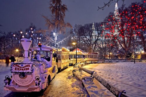 a little train for tourists in a park in a city with snow an christmas lights